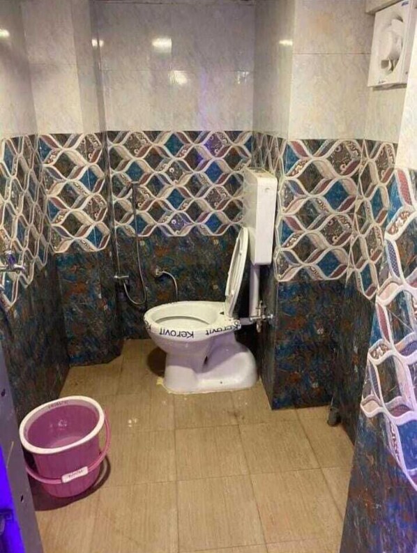 A bathroom with a toilet, a shower, and a tiled wall with a geometric pattern.