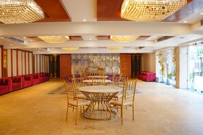Une pièce spacieuse avec une grande table ronde et des chaises, un coin salon avec des canapés rouges et un mur décoratif orné de motifs complexes.
