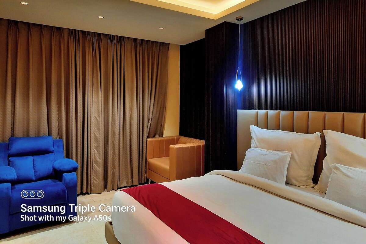 A hotel room with a large bed, two armchairs, a small table, and a curtain.