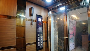 Interior de un ascensor con teléfono, panel de control y puerta de vidrio con un cartel.