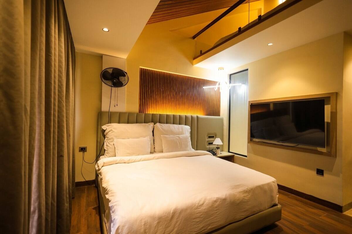 A modern bedroom with a large bed, a ceiling fan, a wall-mounted TV, and a wooden slatted headboard.