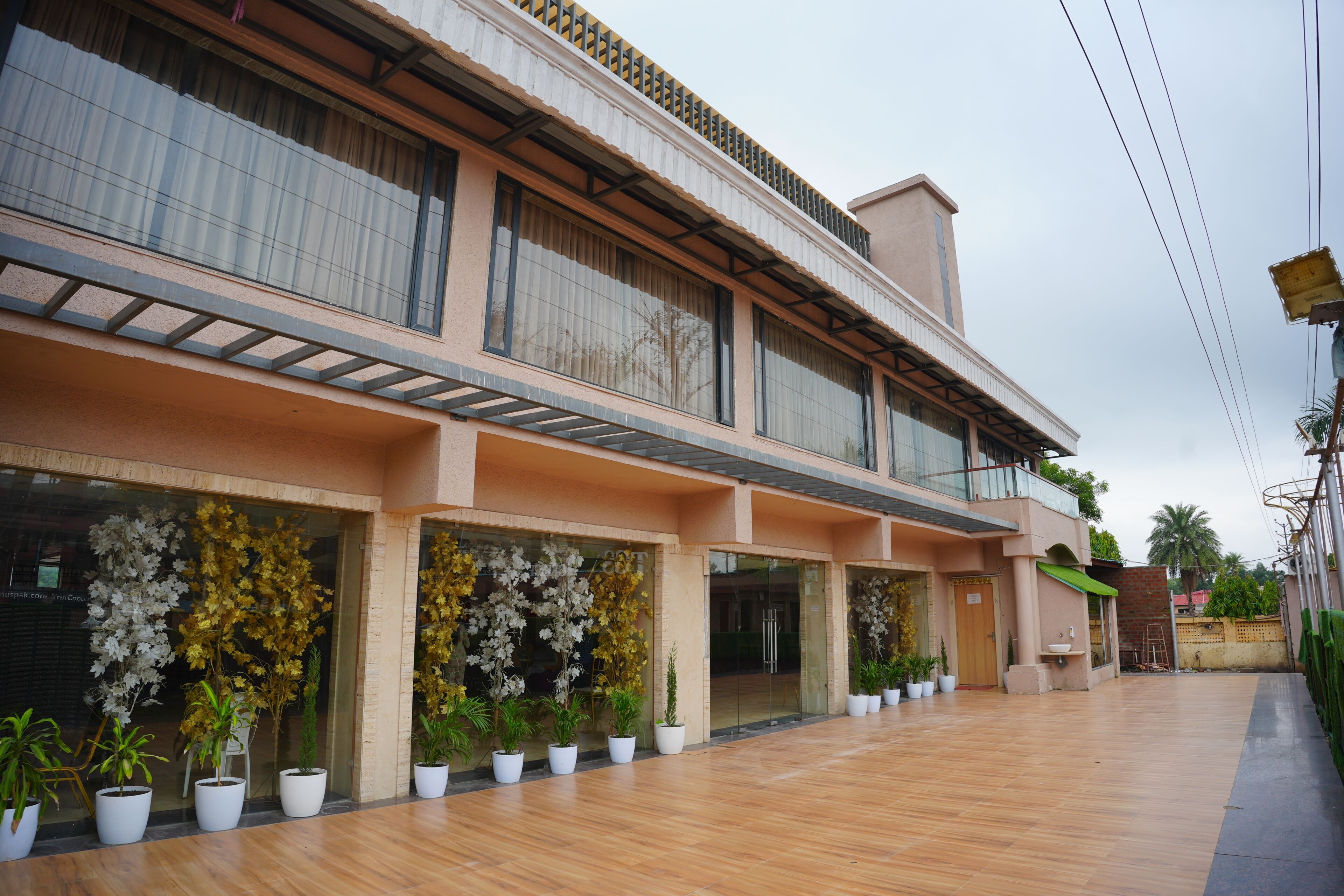A two-story building with a balcony, large windows, and potted plants in front.