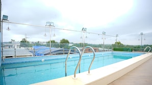 En swimmingpool med flisekant, metalgelændere og udsigt til bygninger i baggrunden.