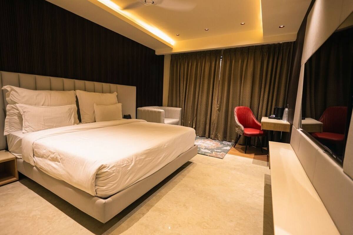 A modern hotel room with a large bed, a desk, a chair, and a mirror.