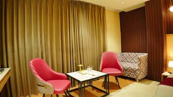 Ein Hotelzimmer mit großem Fenster, zwei roten Stühlen, einem kleinen Tisch, einer Couch und einer Lampe.