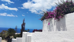 Un edificio blanco con vista al mar, una palmera y flores moradas.