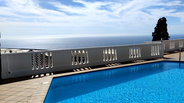 Una piscina con vista al mar, una cerca blanca y una palmera.