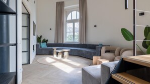 A modern living room with a curved sectional sofa, a round coffee table, and a dining area with a wooden table and benches. - Renovated Luxury Water Tower Within Walking Distance of the Beach/boulevard (Vlissingen)