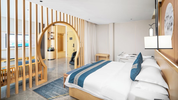 A hotel room with a bed, a desk, and a chair. There is a wooden partition with a circular cutout. - ZEHAI HOTEL (Xi'an)