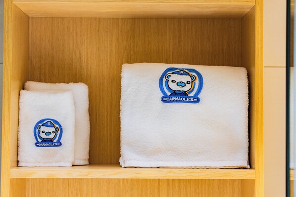 Two white towels with embroidered bear designs on a wooden shelf.