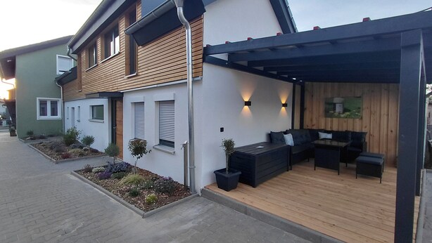 Ein modernes Haus mit Terrasse, Holzboden und Sitzgelegenheit im Freien.