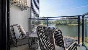 Un balcon avec des fauteuils et une table en osier, donnant sur un lac.