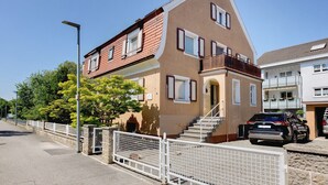 Een woonhuis met twee verdiepingen, een balkon, een geparkeerde auto ervoor en een witte hekken langs de straat.