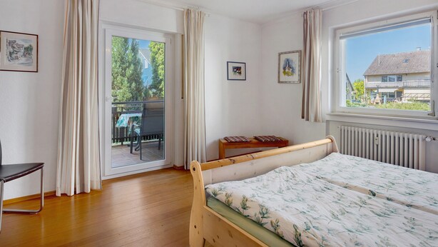 Een slaapkamer met een houten bed, een stoel, een tafel en uitzicht door een glazen deur.