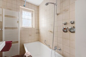 Un baño con bañera, ventana, toallero y cabezal de ducha.