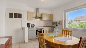 Een moderne keuken met houten kastjes, een eettafel met stoelen en een raam met uitzicht op huizen.