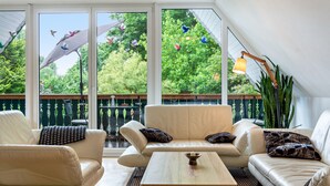 A modern living room with a sofa, armchairs, a coffee table, and large windows with a view of trees and birds. - Apartment 'Landlust' with Shared Terrace, Shared Garden and Wi-Fi (Neudrossenfeld)
