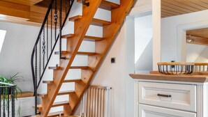 A wooden staircase with a metal railing, a white radiator, a wooden cabinet with drawers, and a wicker basket on the floor. - Apartment 'Landlust' with Shared Terrace, Shared Garden and Wi-Fi (Neudrossenfeld)