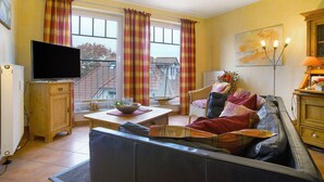 Un salon avec un canapé, une télévision et des fenêtres avec des rideaux.