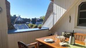 Una mesa de madera con sillas, una botella de vino y una ventana con vistas a casas.
