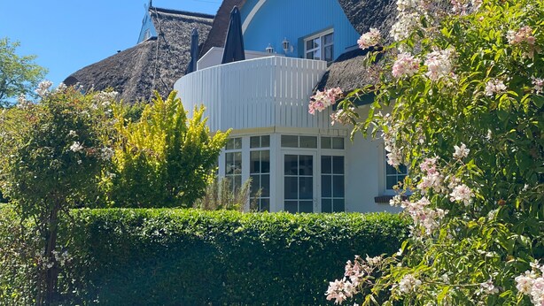 Un edificio con techo de paja, fachada azul y sección con ventanas blancas.