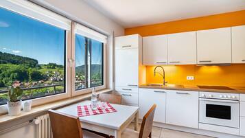 A modern kitchen with white cabinets, a built-in oven, and a window overlooking a scenic landscape.