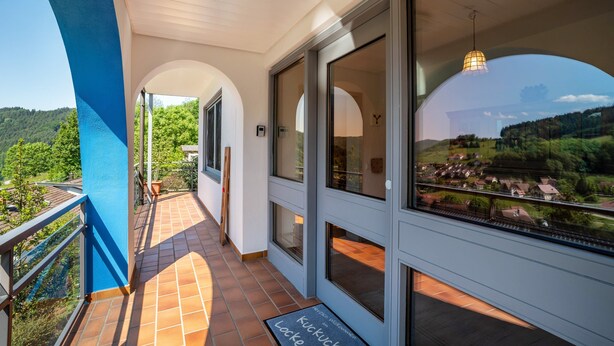 Ein Balkon mit Blick auf ein Dorf, eine Tür mit Glasfenster und eine Fußmatte mit Schrift.
