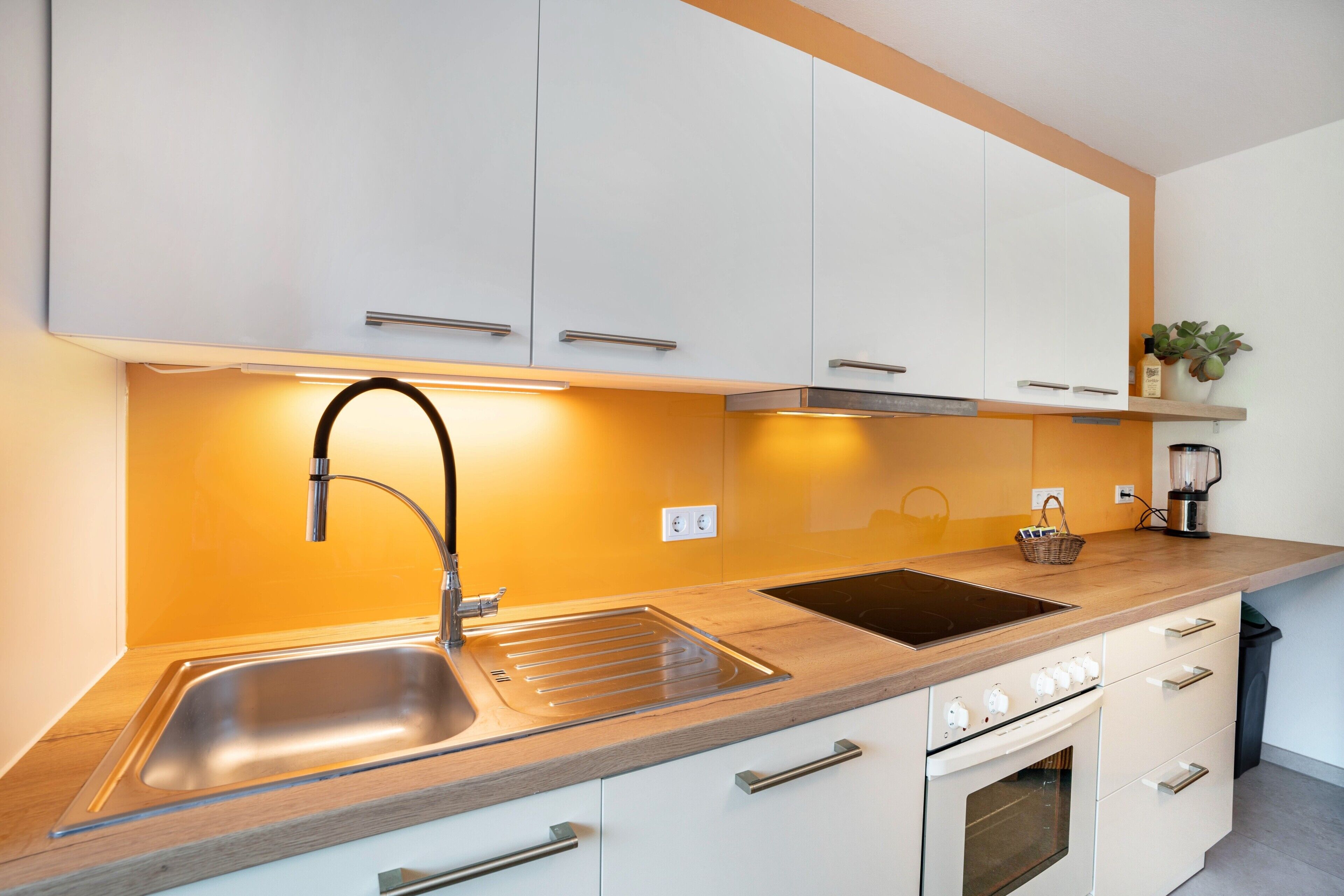 Une cuisine moderne avec des meubles blancs, un évier en acier inoxydable, un four encastré et un plan de travail en bois.