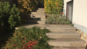 Eine Steintreppe führt zu einem Gebäude, umgeben von verschiedenen Pflanzen und Sträuchern.