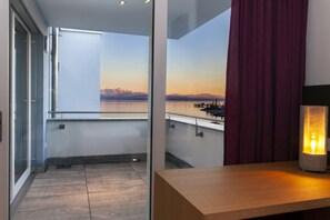 Een balkon met uitzicht op een waterpartij en bergen, een houten tafel met een lamp en een rood gordijn.