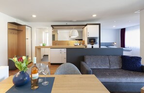Habitación de hotel moderna con zona de comedor, kitchenette y sofá con cojín decorativo.