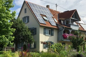 Et hus med to etager, skråtag, solpaneler og en balkon med blomster.