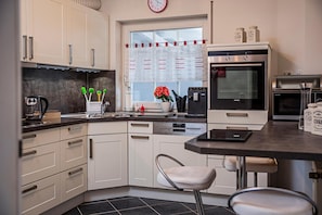 Una cocina moderna con armarios blancos, lavavajillas, horno y ventana con cortina decorativa.