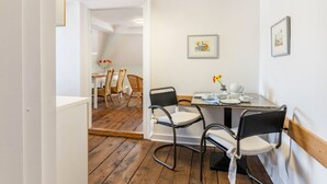 A dining area with a table, chairs, and a view of a room with a bed. - Holiday Apartment in the Former Manor 'Bergblick' with Garden and Wi-Fi (Wurzbach)