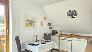 A small kitchen with a dining table, chairs, a microwave, a Bosch dishwasher, and a framed landscape painting.