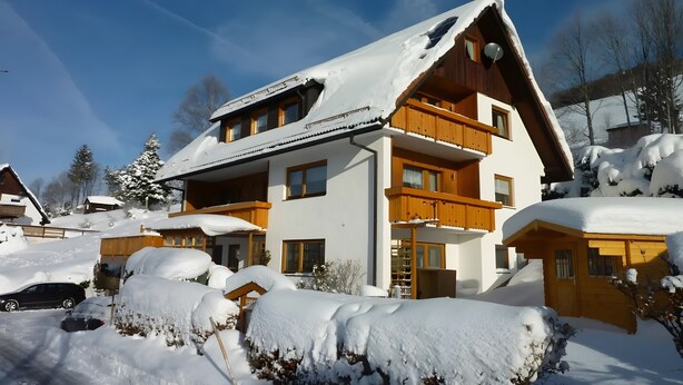 A multi-story chalet with a sloped roof, balconies, and a snow-covered landscape.