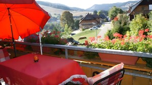 A balcony with a red umbrella, a table with a red tablecloth, and a chair.