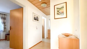 A hallway with wooden doors, a white wall with a framed painting, and a light fixture on the ceiling.