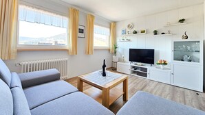 A modern living room with a sofa, a coffee table, a TV, and a kitchen area with cabinets and a shelf.