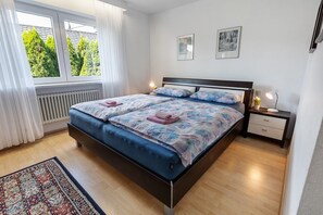 Un dormitorio con cama, mesita de noche, ventana y radiador.