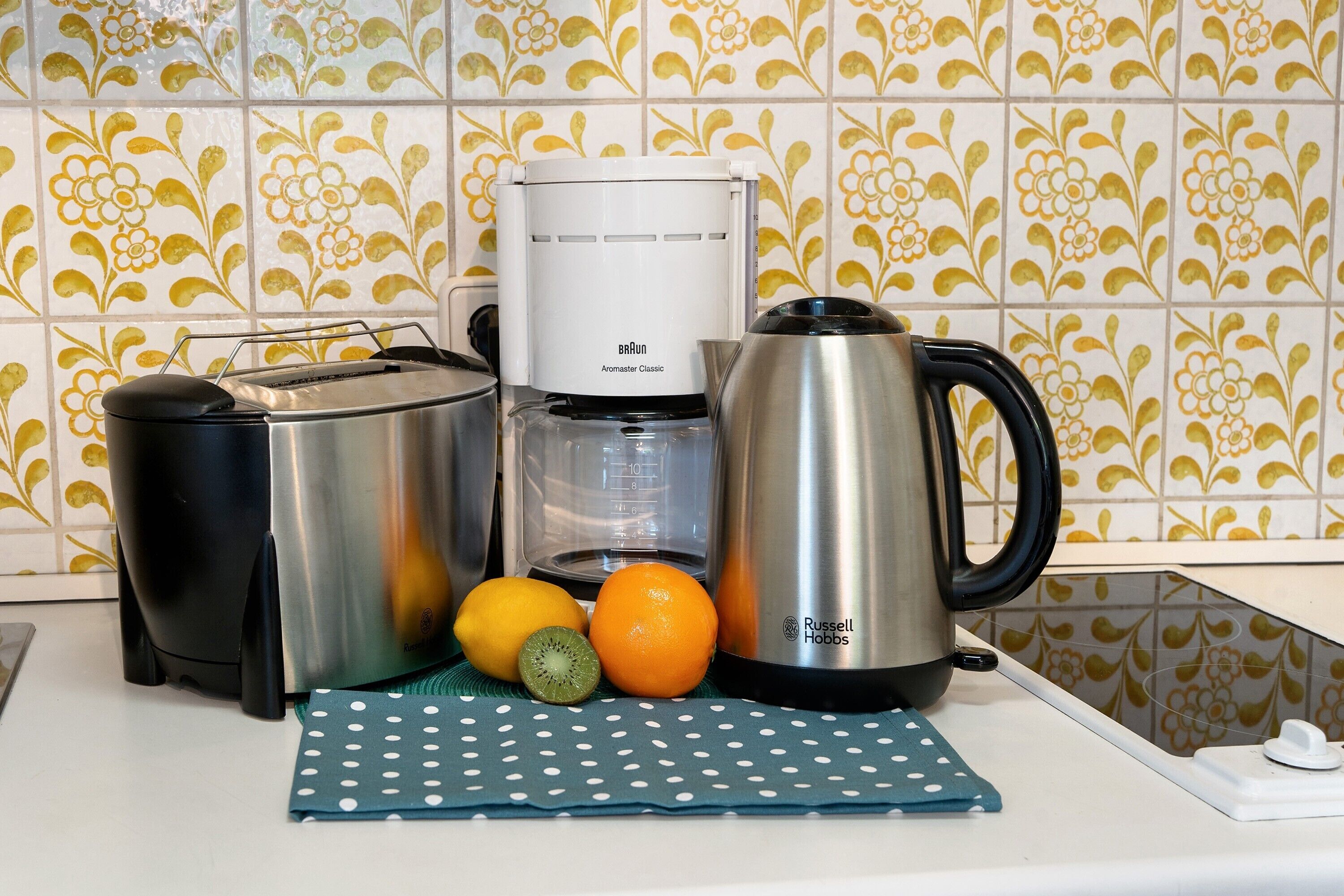 A kitchen counter with a coffee maker, toaster, kettle, and fresh fruits.