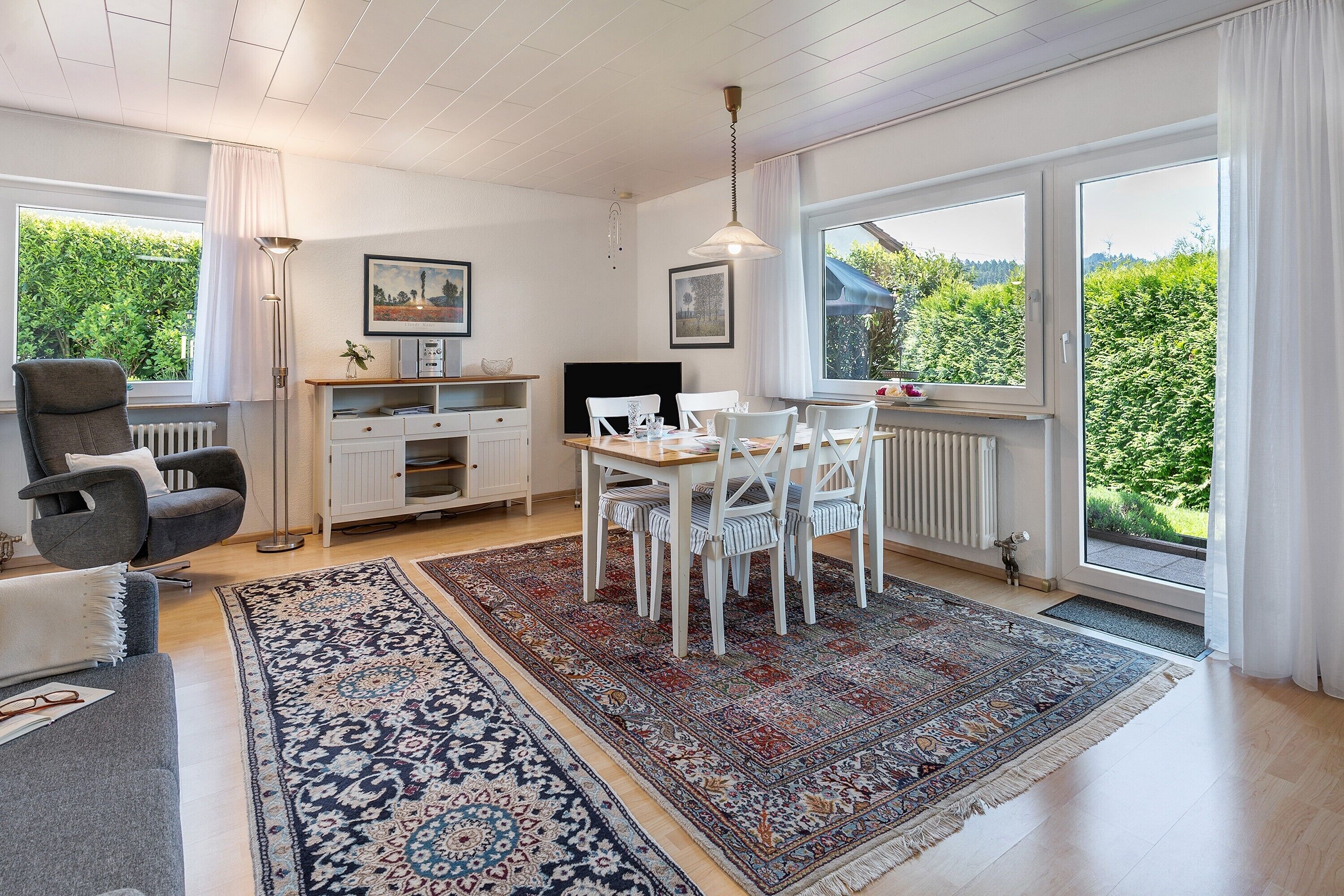 Een moderne woonkamer met een eethoek, grote ramen en uitzicht op groen.
