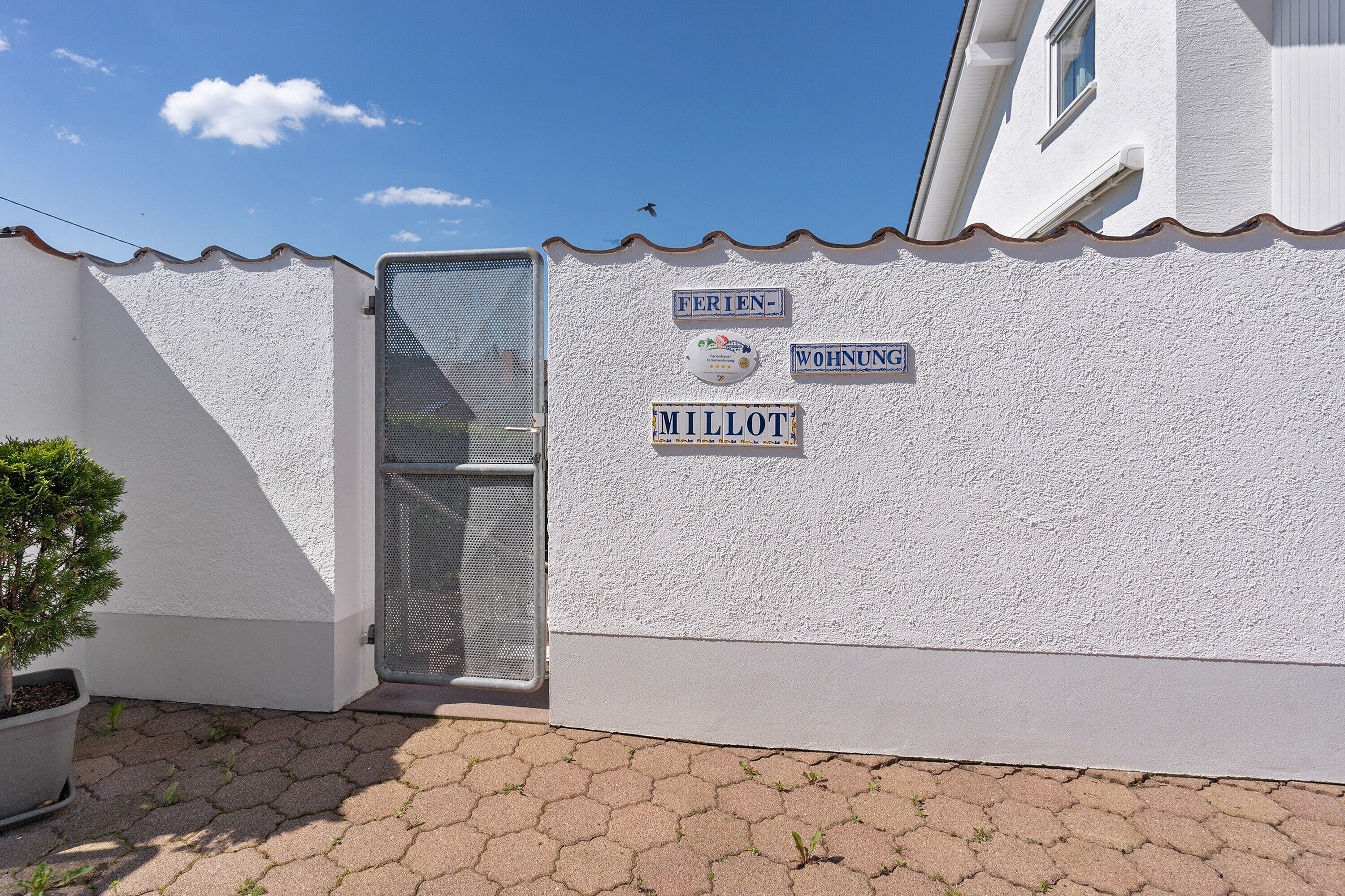 A building with a white exterior, a metal gate, and signs indicating 'FERIEN' and 'MILLOT' on the wall.