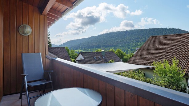 A balcony with a chair and table, wooden walls, and a view of houses and mountains.