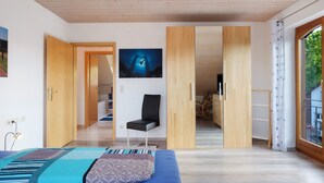 A modern room with a bed, a chair, a painting, and a view through a window.
