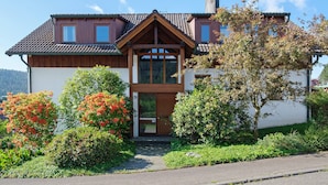A two-story house with a prominent front entrance, a sloped roof, and a small balcony.