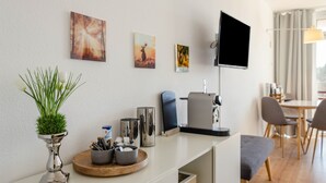Ein modernes Hotelzimmer mit Flachbildfernseher, Kunstwerk an der Wand, einer kleinen Pflanze und einer Kaffeestation.