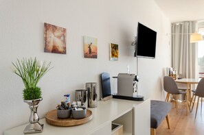 A modern hotel room with a flat-screen TV, artwork on the wall, a small plant, and a coffee station. - Apartment 'Seeblickappartement Eure Zeit' with Lake View, Balcony and Wi-Fi (Goslar)