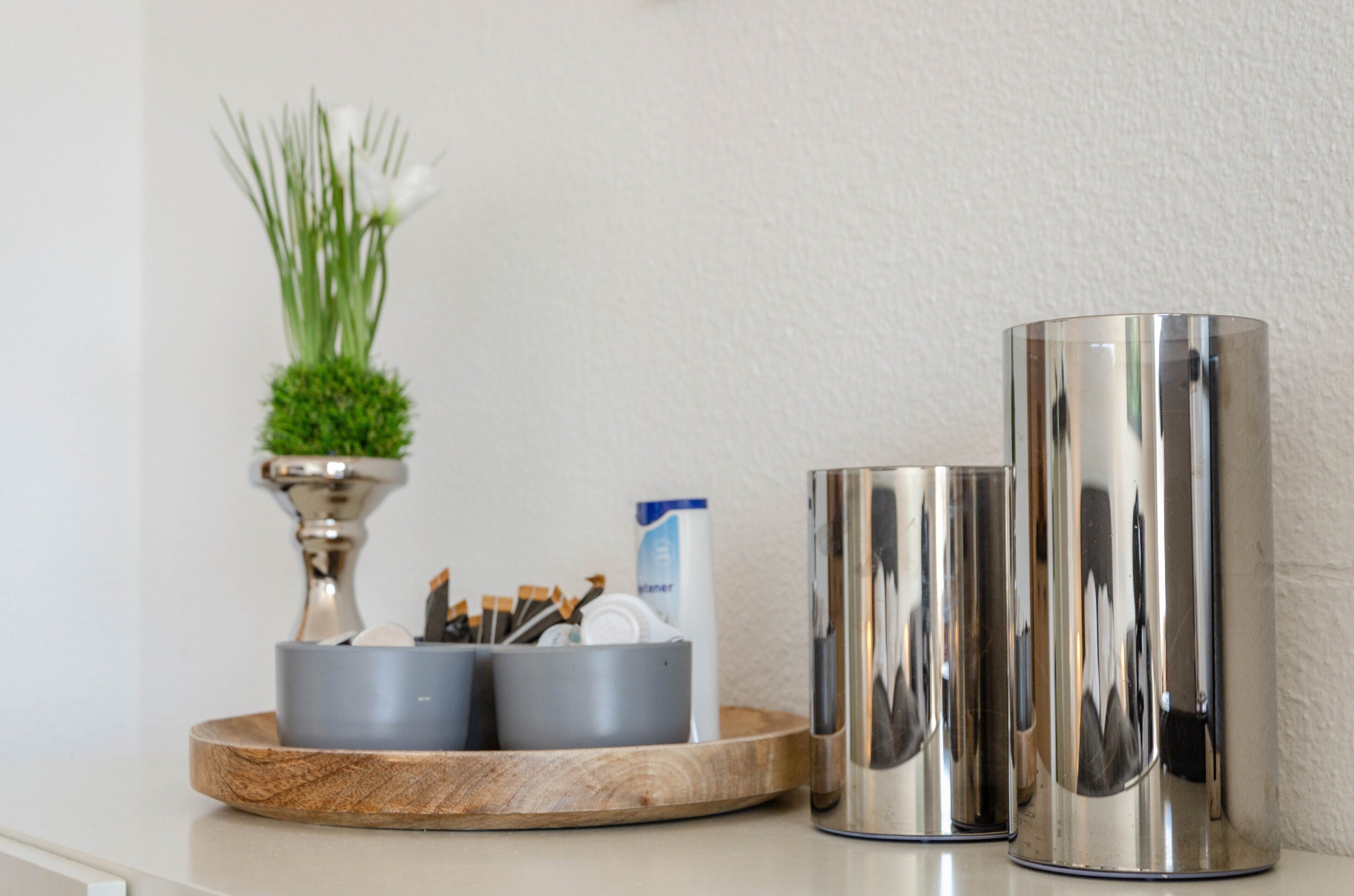 Una encimera de cocina con un jarrón decorativo, utensilios de cocina y dos recipientes de acero inoxidable.