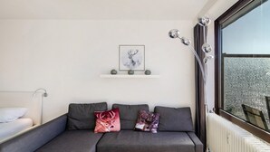 A modern living room with a grey sofa, two decorative pillows, a framed deer artwork, a white radiator, and a window with a view.